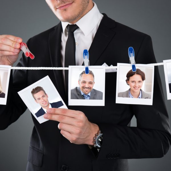 Midsection of businessman selecting candidate from clothesline against gray background